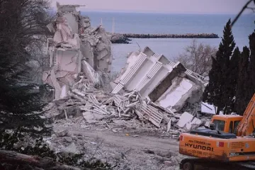 Оцелял работник със скъсани дрехи помага в разчистването на отломките